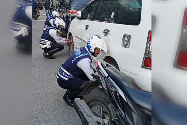 GEMBOSI: Petugas Dishub Medan menggembosi ban mobil yang parkir sembarangan.