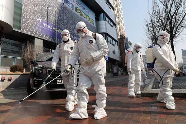 SIAGA COVID-19 Sejumlah petugas mengenakan pakaian pelindung diri dan menenteng semprotan disinfektan di sebuah pasar Kota Daegu, Korea Selatan, Minggu (23/2). Pemerintah Korsel kini meningkatkan kewaspadaan terhadap COVID-19 .