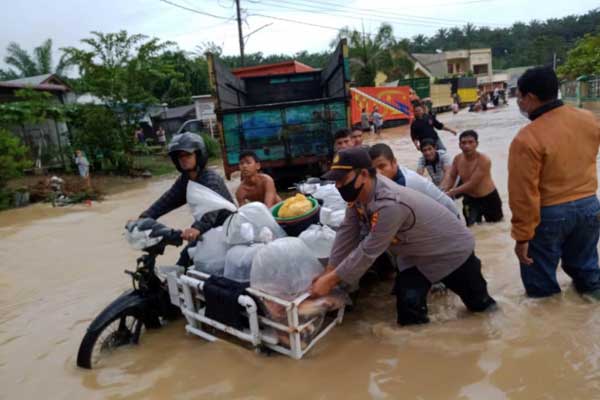 BANTU: Seorang personel kepolisian membantu warga mendorong becak motornya yang mogok karena terendam banjir.