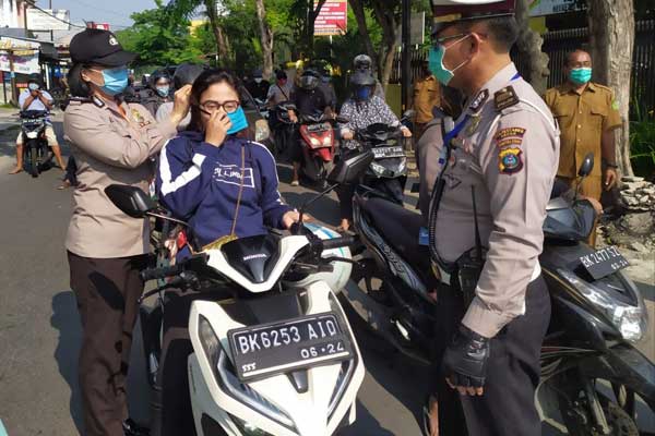 PAKAIKAN MASKER: Polisi Wanita (Polwan) Polsek Medan Helvetia memakaikan masker kepada pengendara sepeda motor yang melintas di Jalan Matahari Raya Medan, Selasa (21/4).