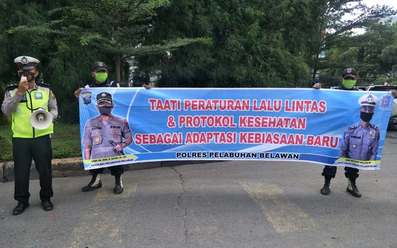 SPANDUK: Petugas Satlantas Polres Pelabuhan Belawan membentang spanduk berisi imbauan untuk mematuhi lalu lintas dan protokol kesehatan.fachril/sumutpos.