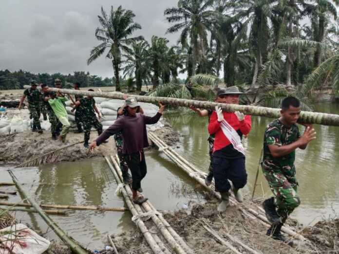 PERBAIKI: Prajurit TNI saat memperbaiki tanggul yang jebol di Langkat. (Istimewa)