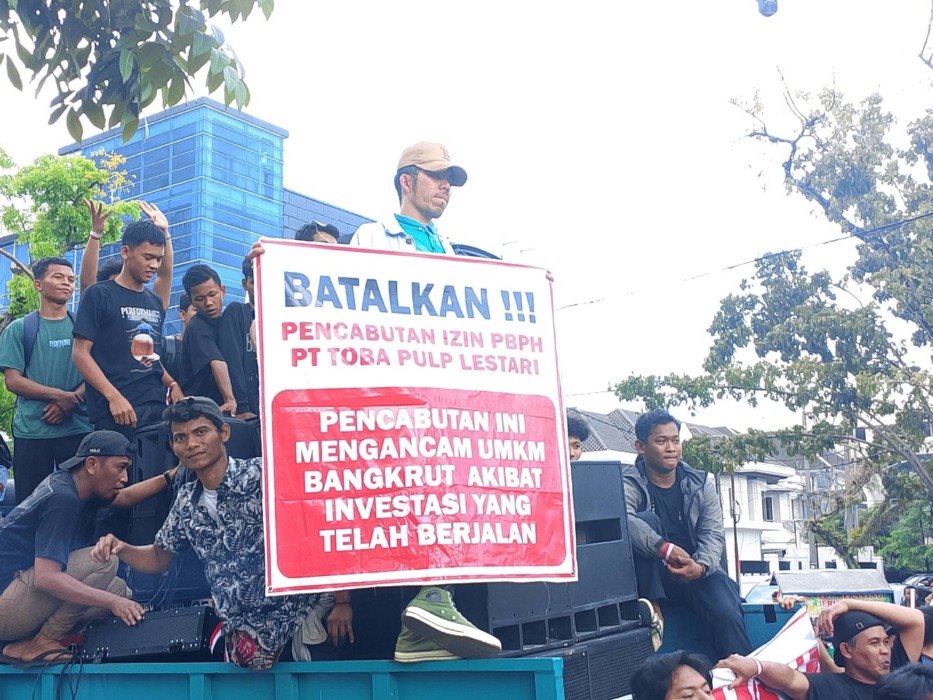 BENTANG SPANDUK: Seorang masa aksi membentangkan spanduk berisi pencabutan izin PBPH PT.TPL mengancam UMKM dan investasi yang sedang berjalan, yang ditunjukan di depan Kantor Gubernur Sumatera Utara, Jumat (18/4/2026). Foto : Ihsan Syahreza