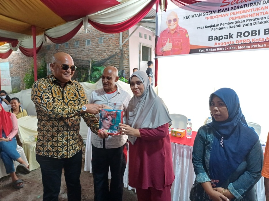 CENDERAMATA: Ketua Fraksi PDI Perjuangan DPRD Kota Medan, Robi Barus SE M.AP memberikan cenderamata kepada warga saat menggelar Sosialisasi Perda Kota Medan No.9 Tahun 2017 di Medan Barat, Minggu (19/4/2026) sore. (Markus Pasaribu/Sumut Pos)
