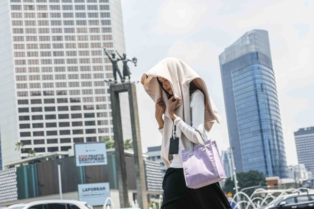 CUACA PANAS: Seorang pejalan kaki melindungi kepalanya dengan jaket untuk menghindari cuaca panas di salah satu kota. Sedangkan di Kota Medan, cuaca panas mencapai 36 derajat celsius.