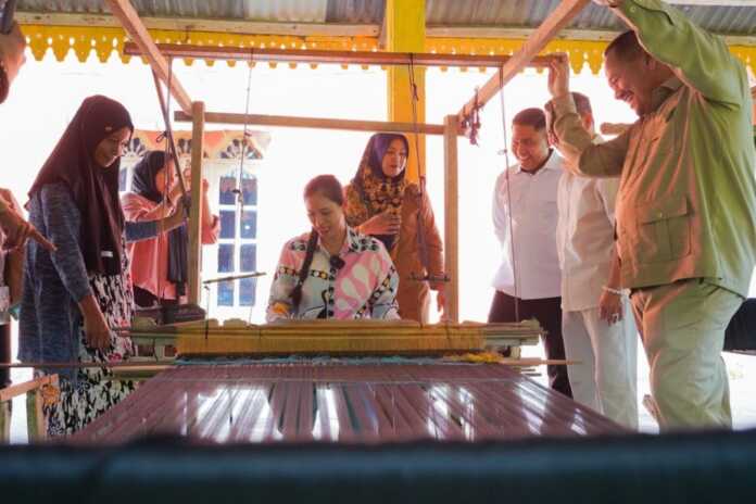 MECOBA MENENUN:  Bupati Batubara H Baharuddin bersama Bendahara Gerindra Sumut, Meriyawaty saat mencoba proses menenun di Kampung Tenun ‘Tonun’ Desa Pematanggenting, Talawi, Senin (30/3).