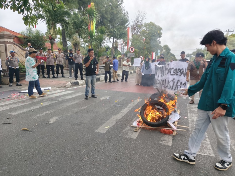 ORASI: Mahasiswa HMI Cabang Pematangsiantar-Simalungun melakukan aksi bakar ban dan menyampaikan orasi saat unjuk rasa di Jalan Sutomo, depan Kantor DPRD Kota Tebing Tinggi, Senin (29/6/2026).