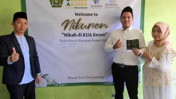 Nikah di KUA Medan FOTO BERSAMA: Kepala KUA Kecamatan Medan Perjuangan, H Ramlan (kiri) berfoto bersama pengantin yang baru nikah di Kantor KUA kecamatan Medan Perjuangan, Jalan Pendidikan dengan menuliskan impuan di papan wedding wish board.(Tomi Sanjaya Lubis/Sumut Pos)