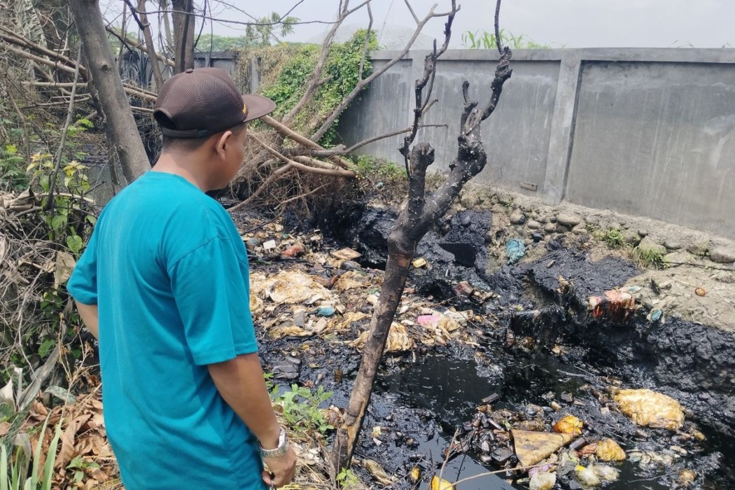 BEKAS KEBAKARAN: Kepala Dusun (Kadus) 15, Rudianto, melihat keadaan parit di depan rumah warga yang terbakar diduga karena banyaknya limbah minyak yang menggenang, Sabtu (22/8).(net)